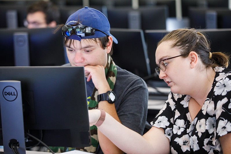 Picture of two students helping each other in front of a PC